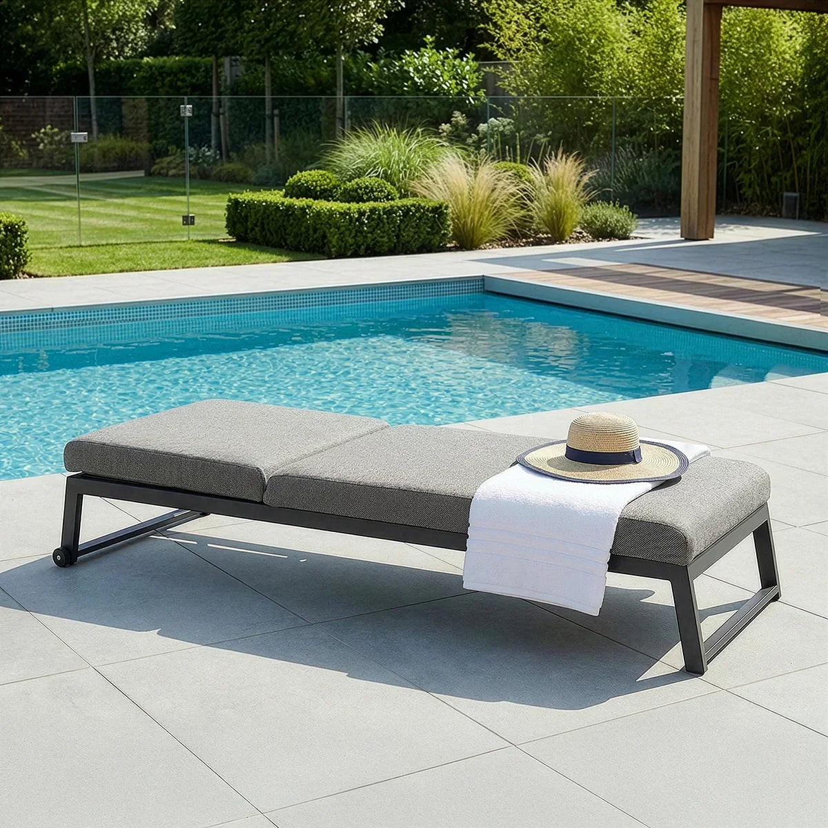 Grey outdoor sun lounger with cushion beside swimming pool, hat and towel on seat