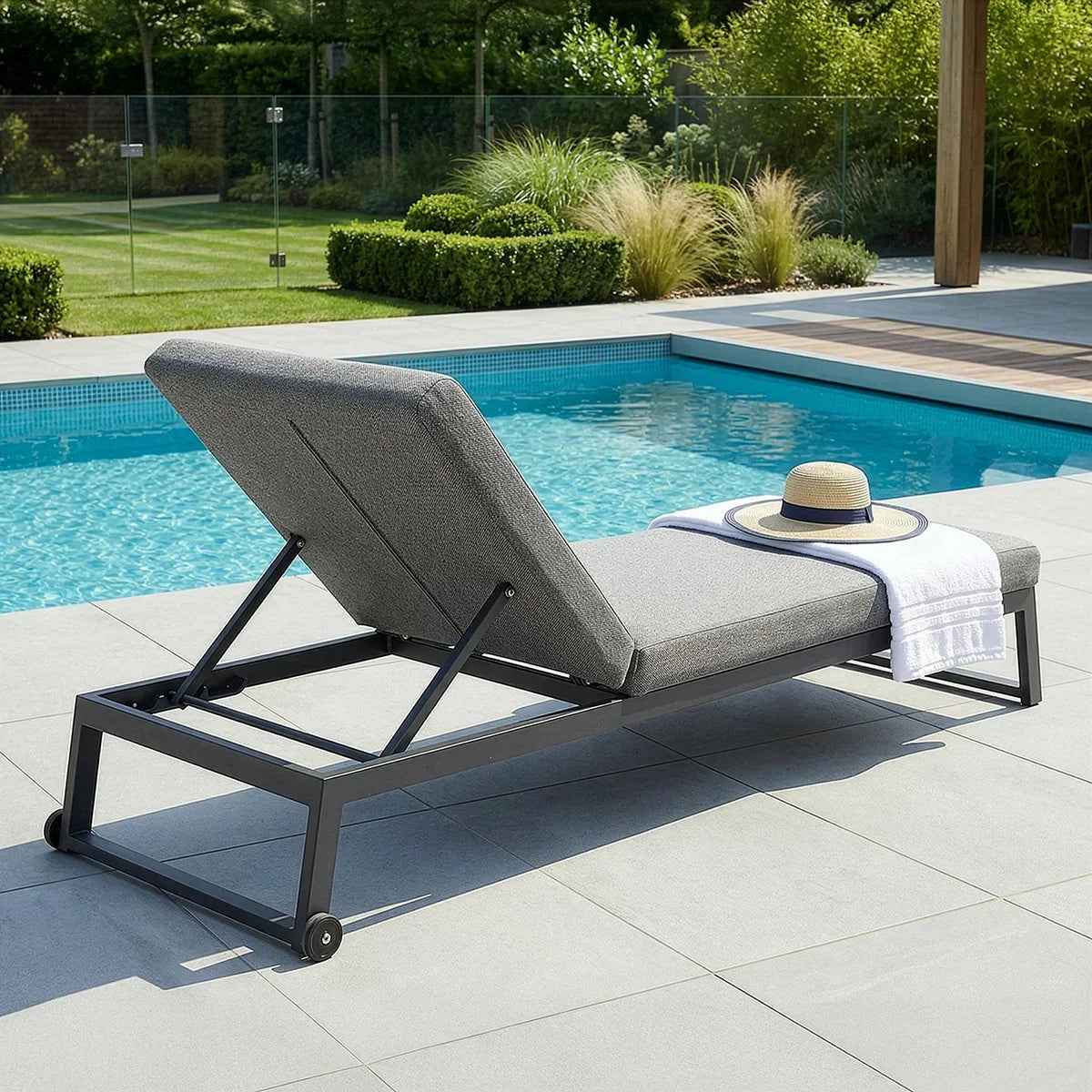 Grey aluminium sun lounger with adjustable backrest by pool, hat and towel on seat
