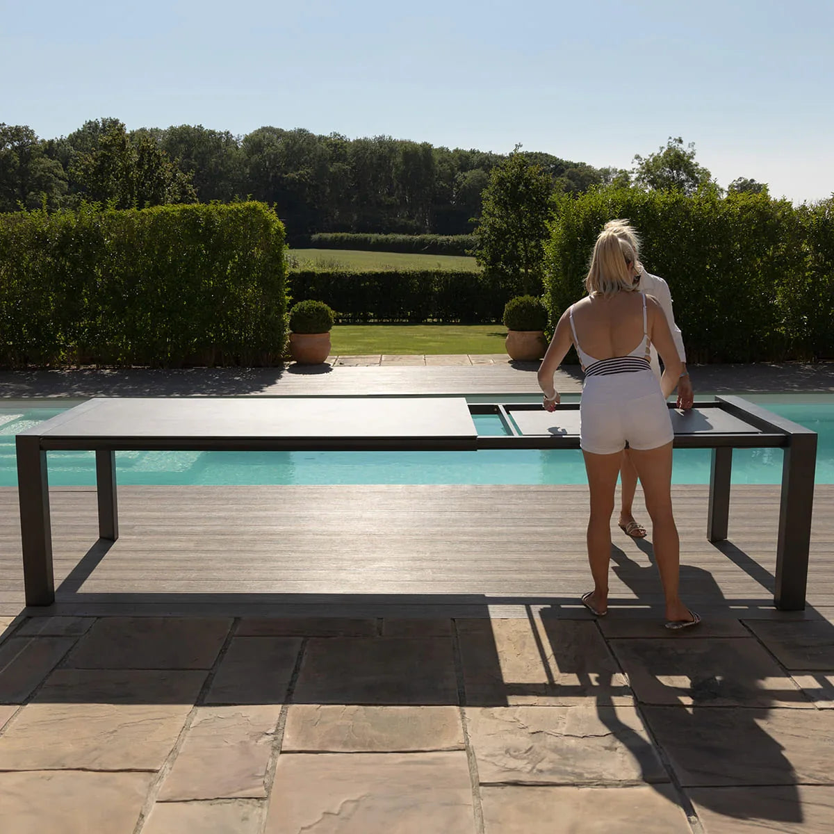 Outdoor extending dining table by pool with two people adjusting tabletop