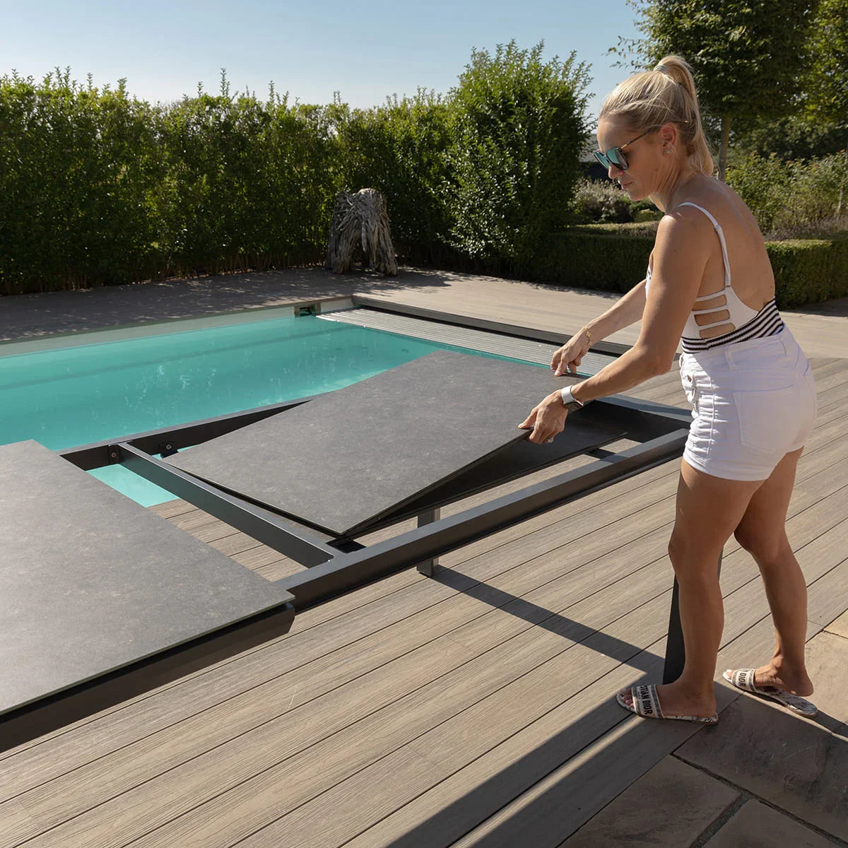 Extending outdoor dining table with dark top by swimming pool on wooden decking