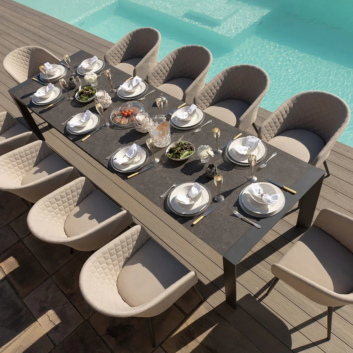 Outdoor dining table set with eight cushioned chairs by pool, tableware and serving dishes