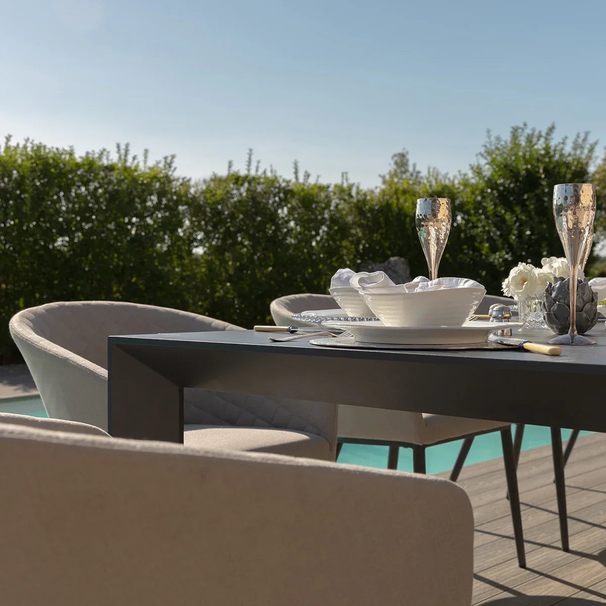 Modern outdoor dining set with grey cushioned chairs and table by pool, tableware arranged
