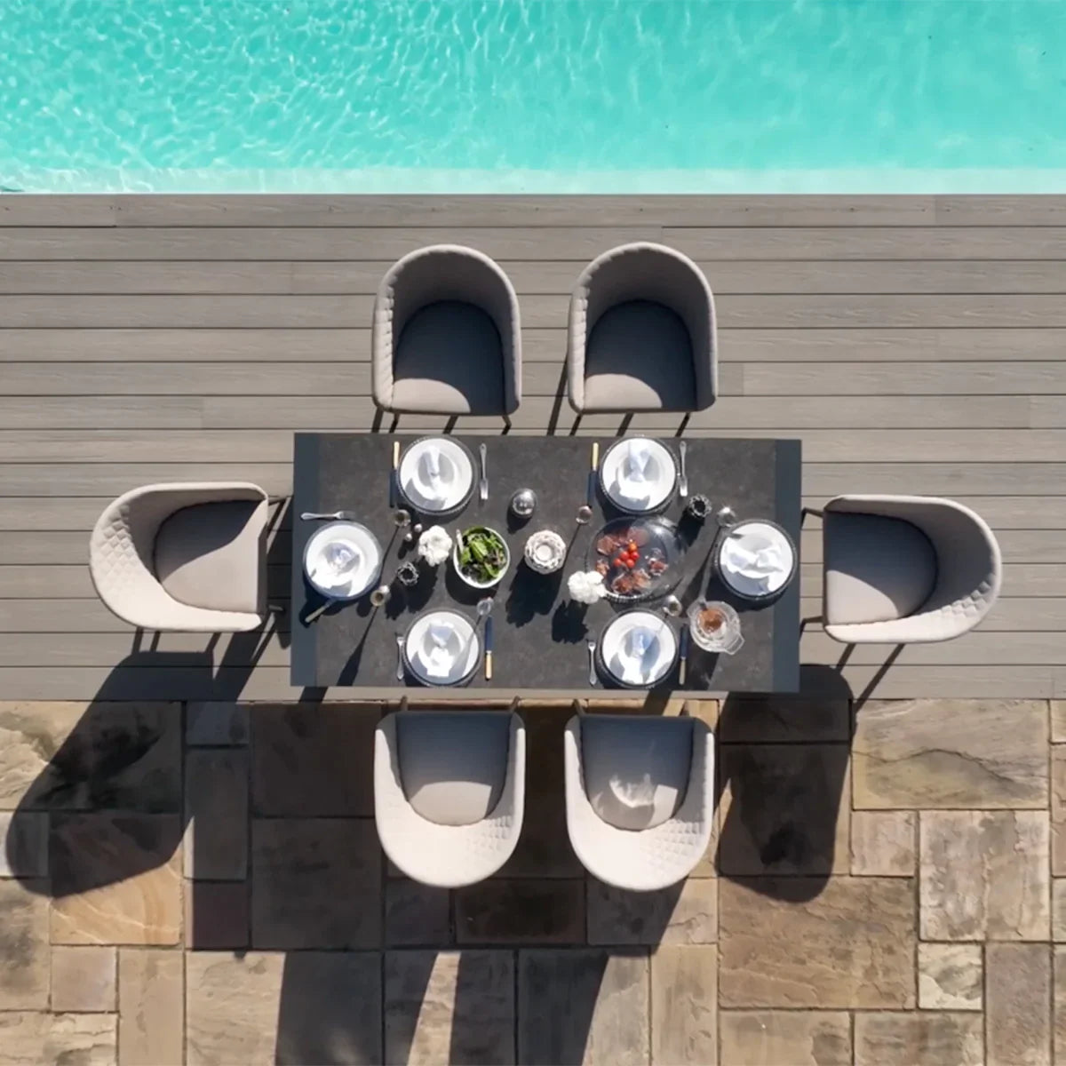 Outdoor dining set with six grey cushioned chairs and rectangular table by swimming pool
