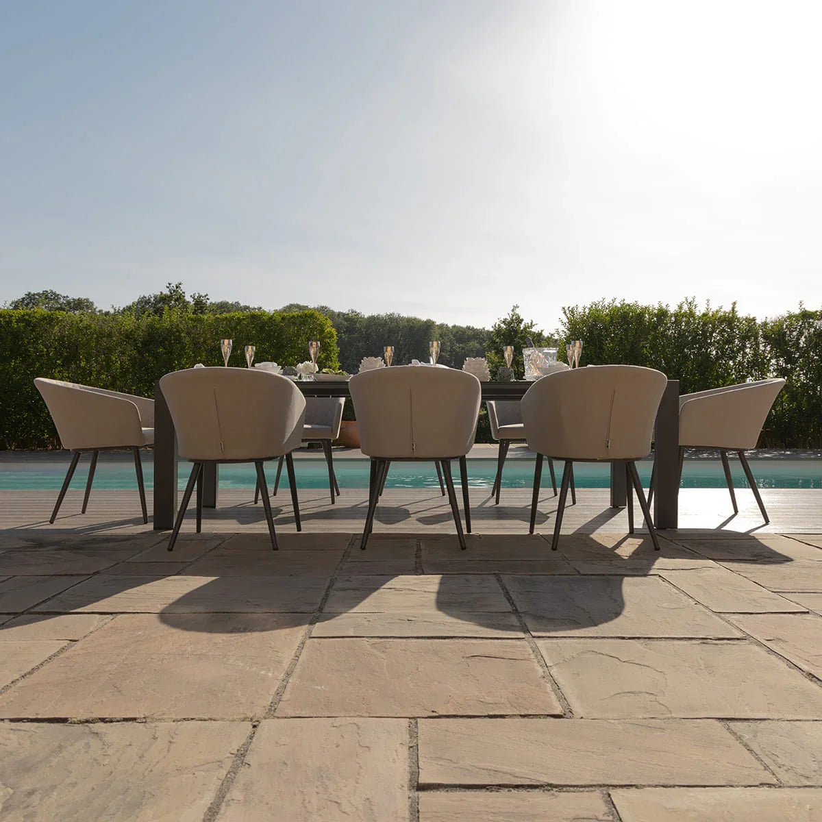 Modern outdoor dining set with cushioned chairs by a pool on a stone patio