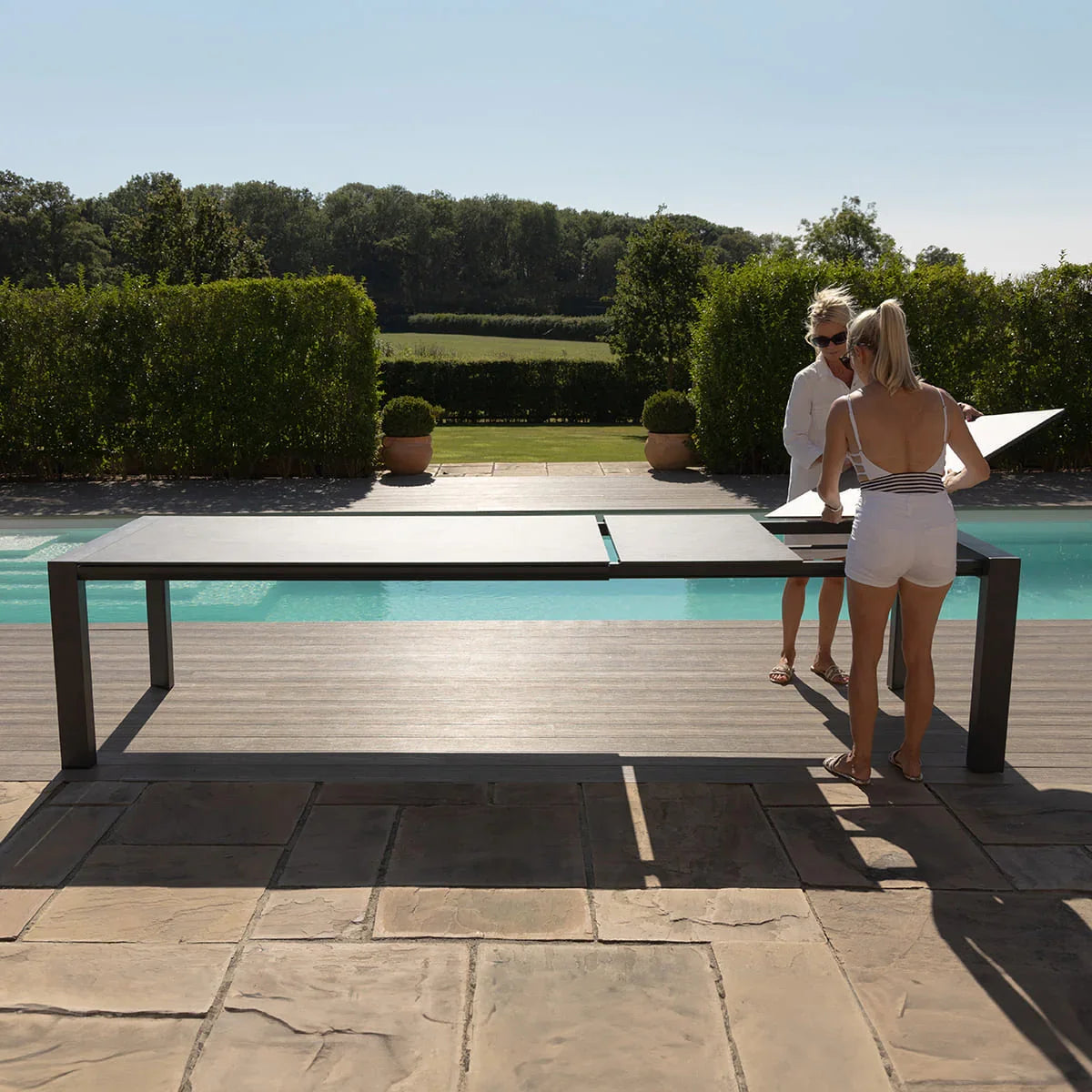 Outdoor extending dining table by pool with two people assembling top panels
