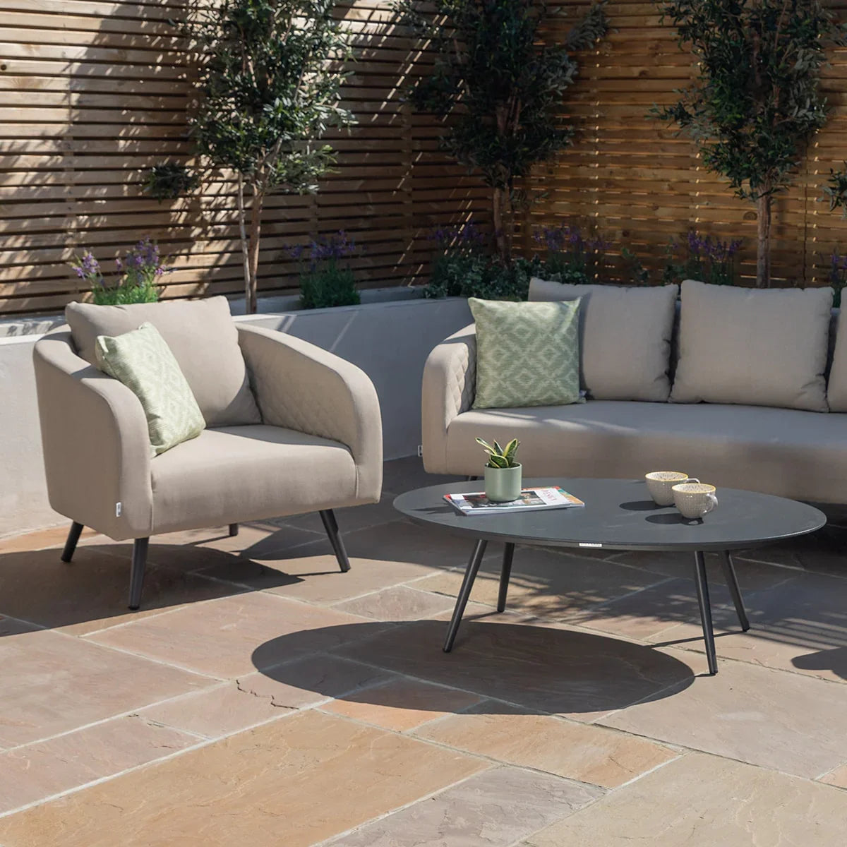 Outdoor patio sofa set with beige cushions, armchair, black coffee table and green pillows