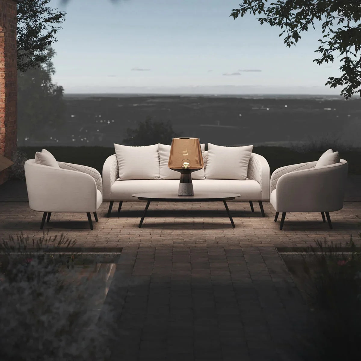 Outdoor sofa set with cream fabric armchairs, coffee table, and lantern on patio at dusk