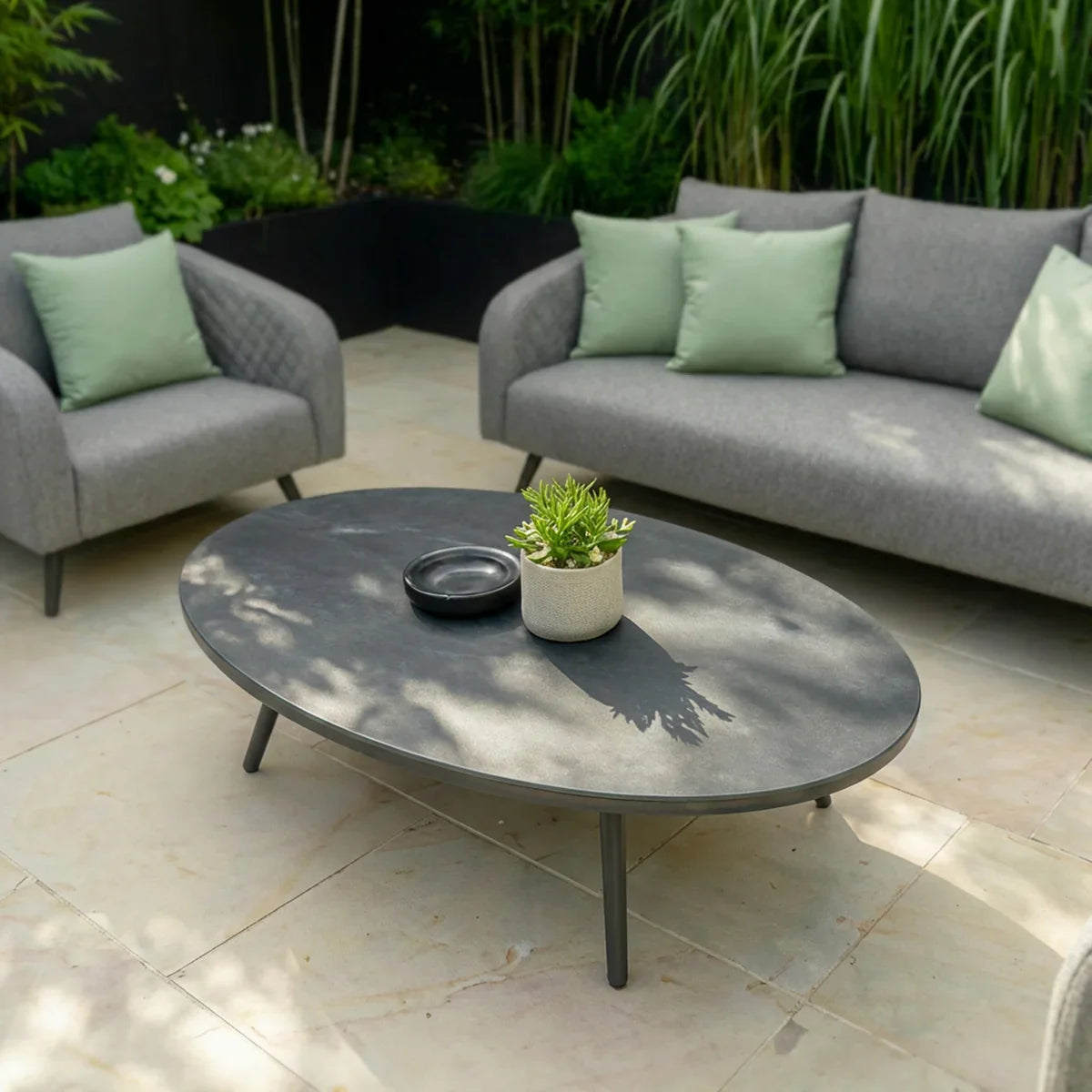 Grey outdoor sofa set with armchair and oval coffee table on a stone patio