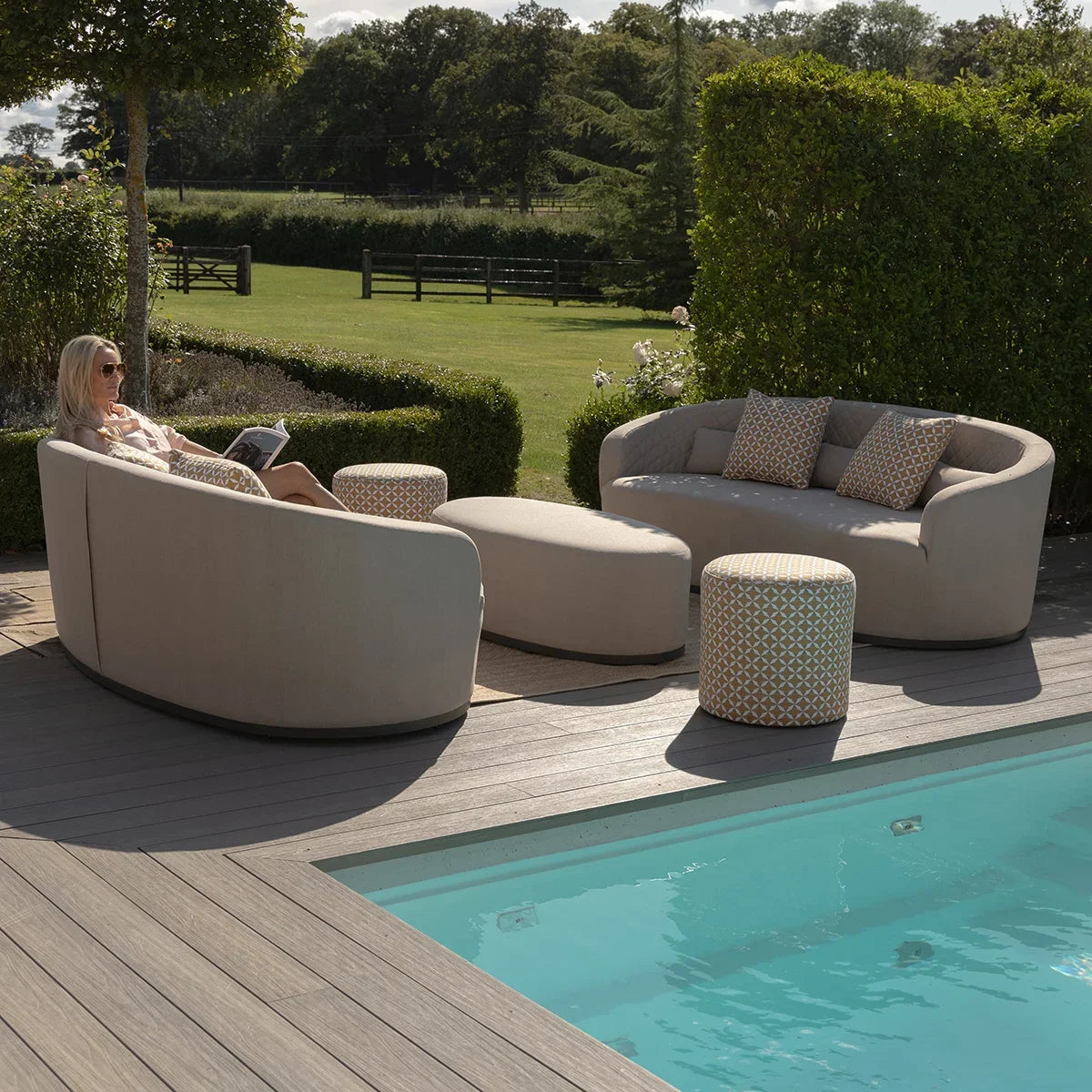 Beige outdoor sofa set with ottoman and stools by poolside, patterned cushions included