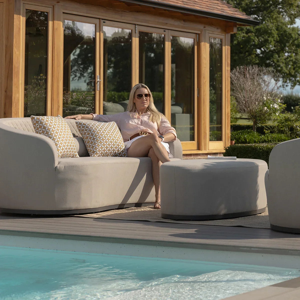 Modern outdoor sofa set with beige upholstery and geometric cushions beside a pool