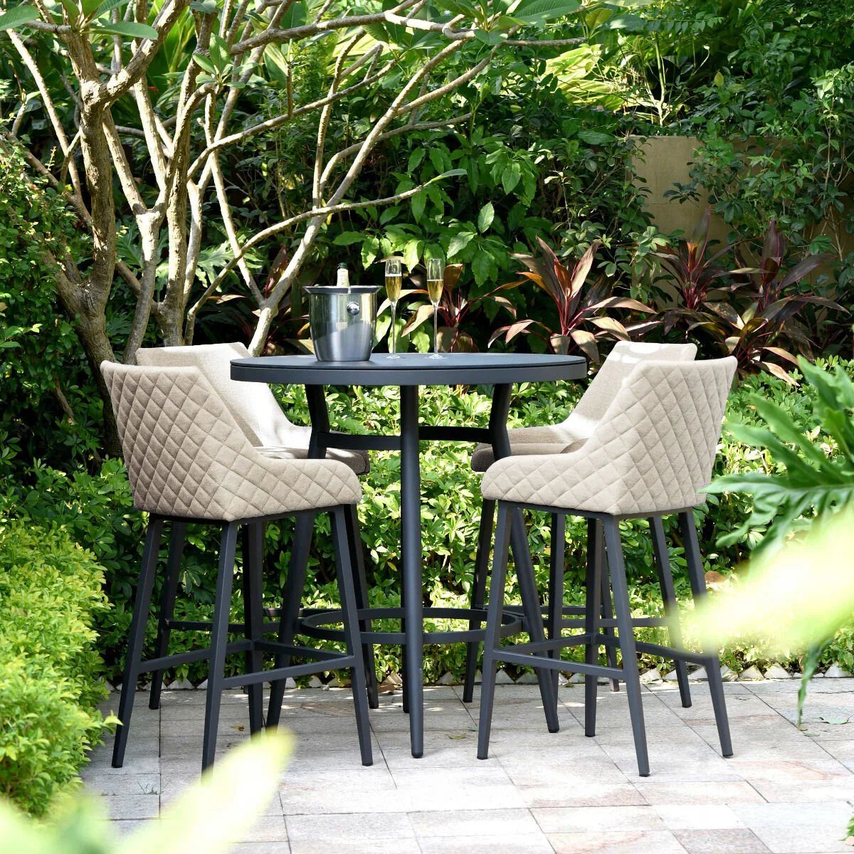 Outdoor bar table set with three quilted beige bar stools in a garden patio setting