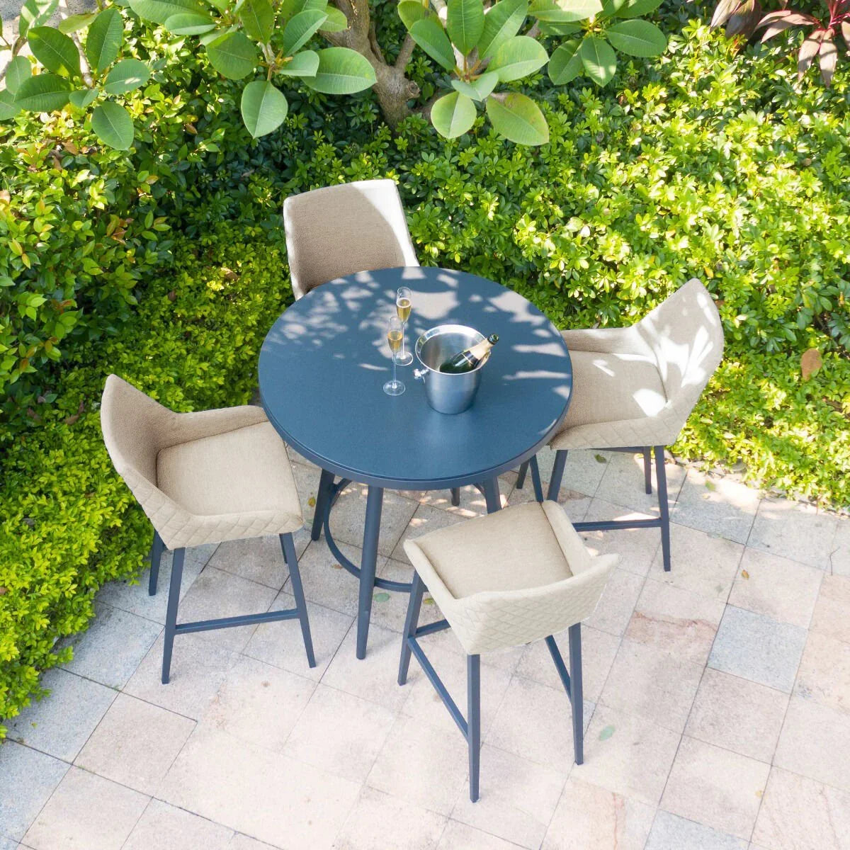 Round outdoor bar table with four beige cushioned chairs on patio with champagne bucket