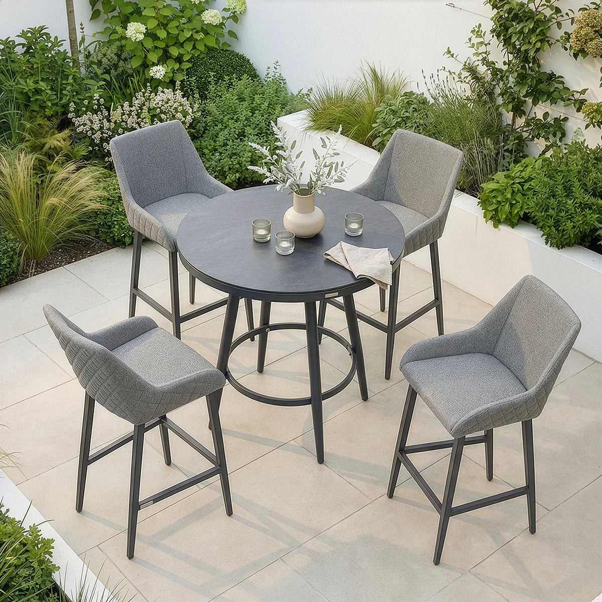 Grey outdoor bar table set with four cushioned bar stools on tiled patio