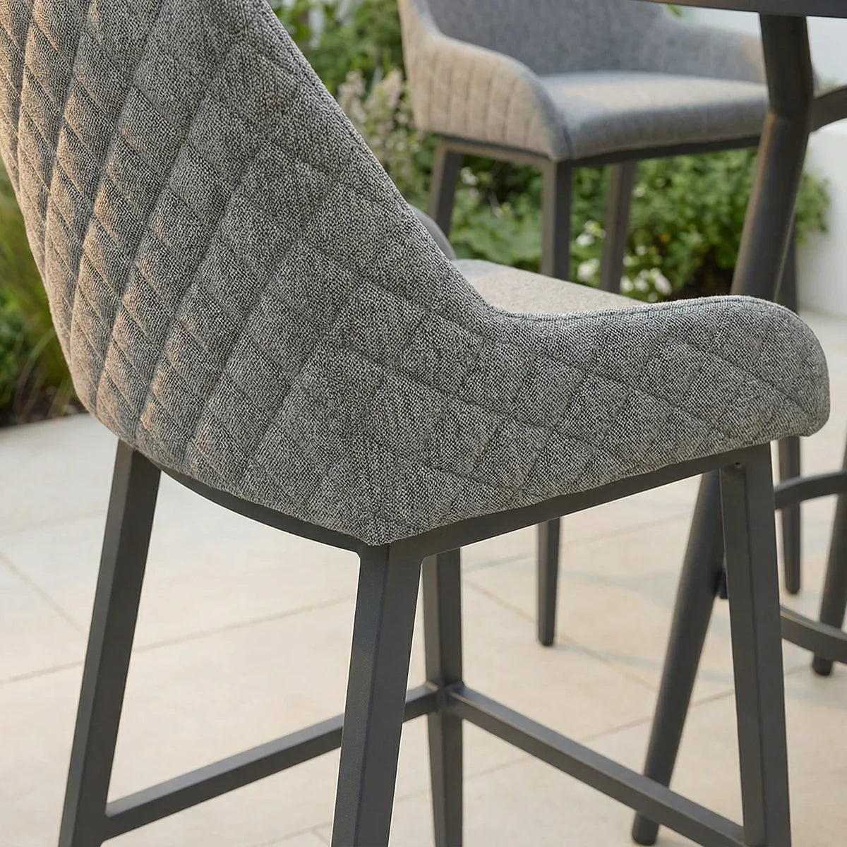 Grey fabric bar stool with quilted backrest and black metal legs on patio