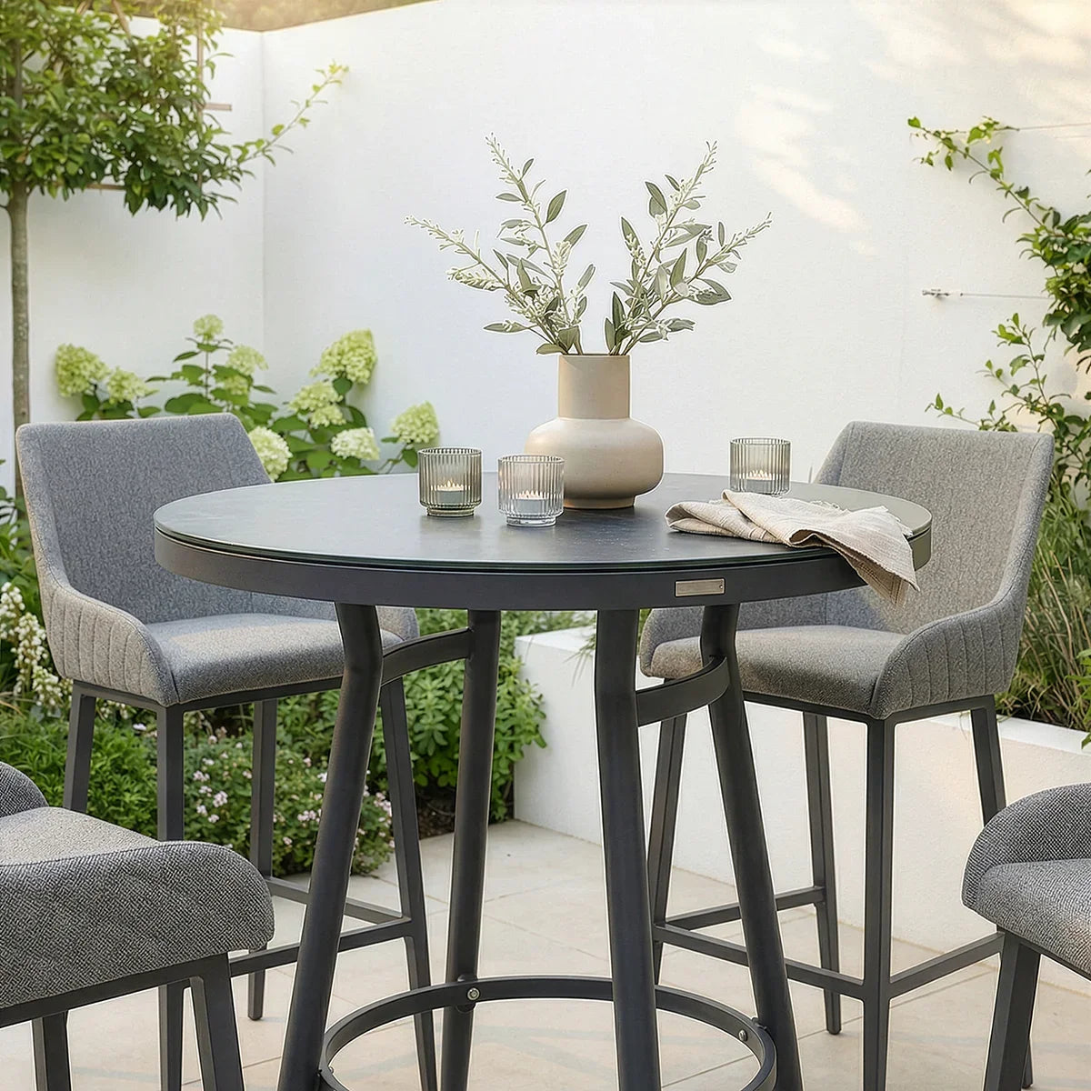 Round grey bar table with four upholstered stools in a modern garden patio setting
