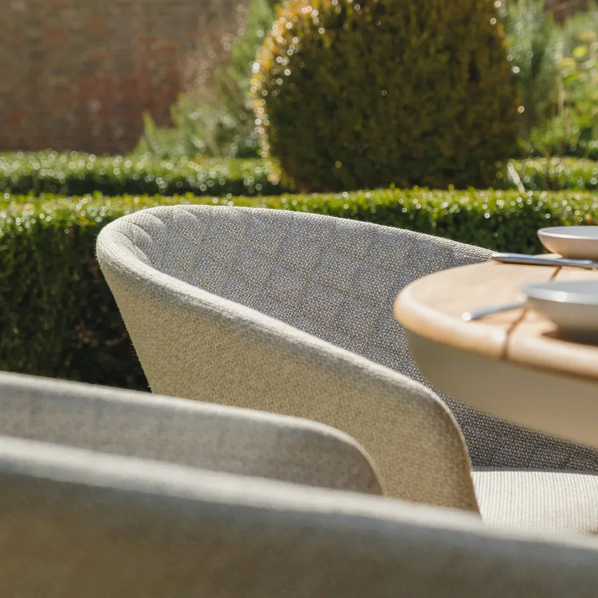 Beige outdoor dining chair with textured fabric beside round wooden garden table