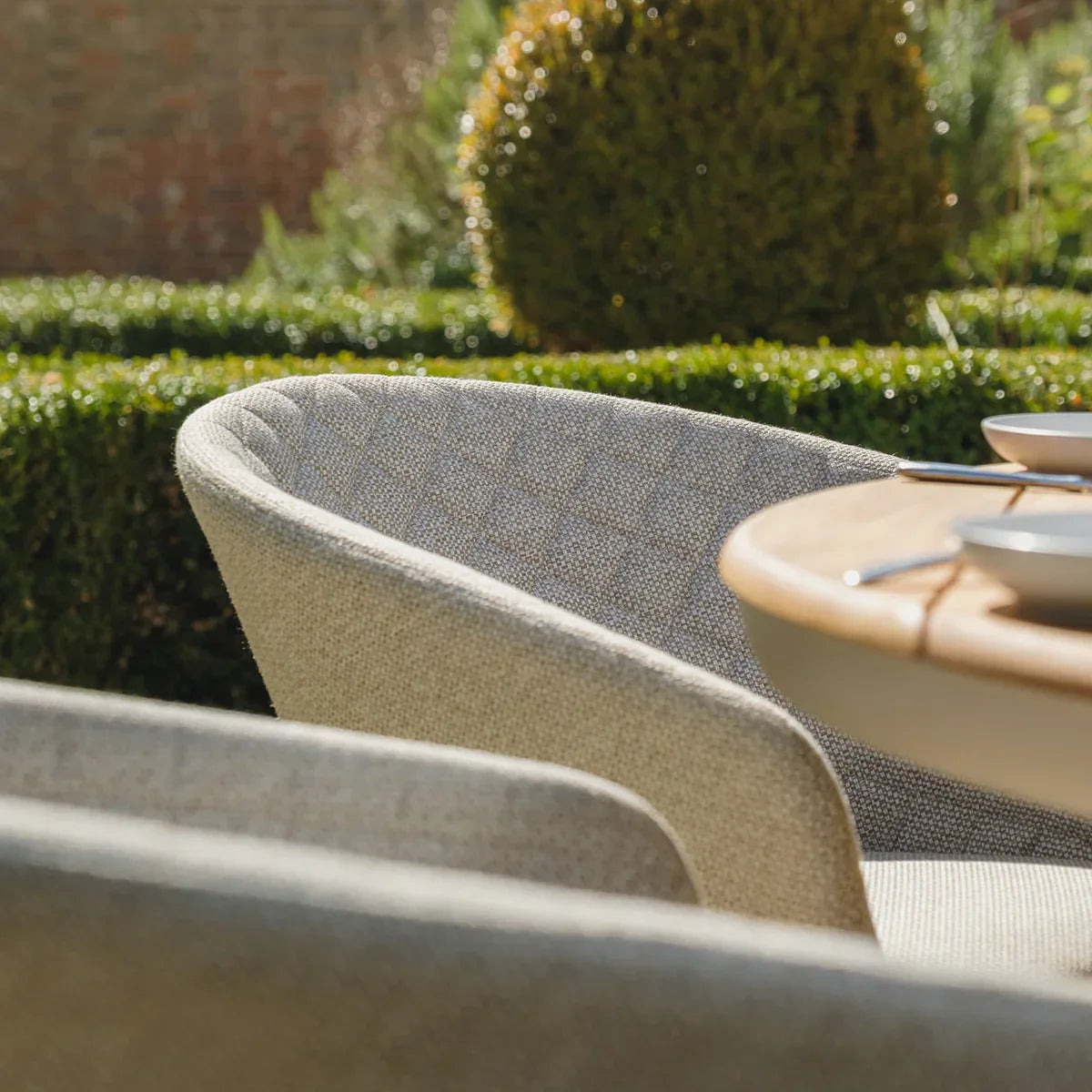 Outdoor fabric dining chair with quilted backrest beside round wooden garden table