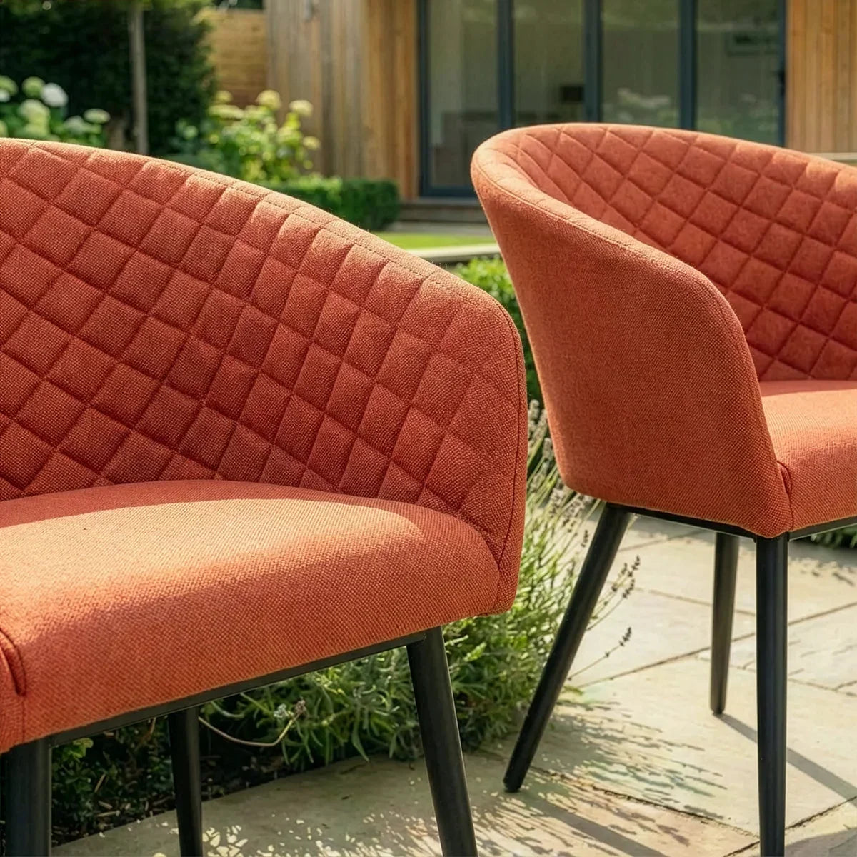 Rust orange fabric dining chairs with quilted backrest and black legs on patio