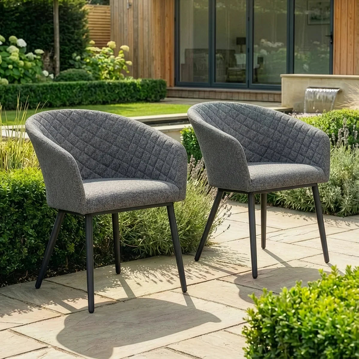 Set of two grey fabric garden chairs with black legs on patio surrounded by greenery