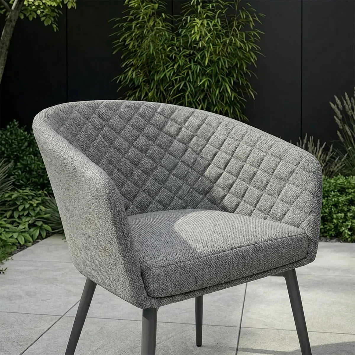 Grey fabric armchair with quilted backrest on patio, surrounded by green garden plants