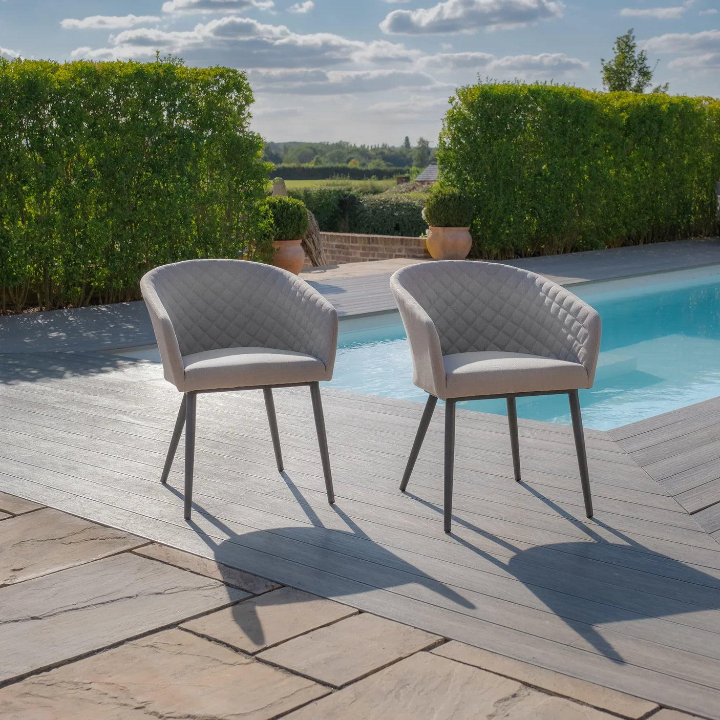 Pair of grey outdoor armchairs with quilted seats by a pool on decking