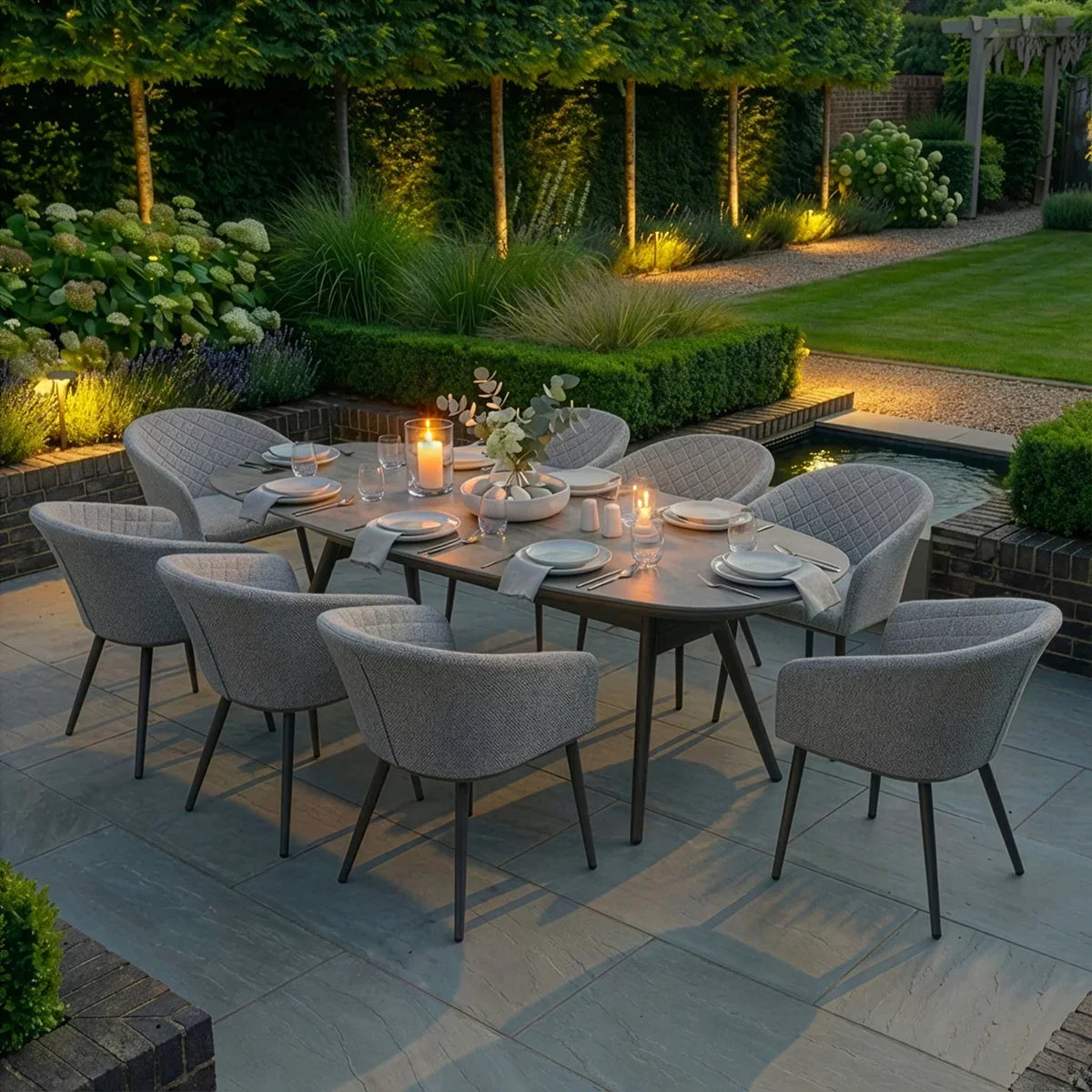 Eight seater outdoor dining set with grey cushioned chairs on a patio, evening garden scene