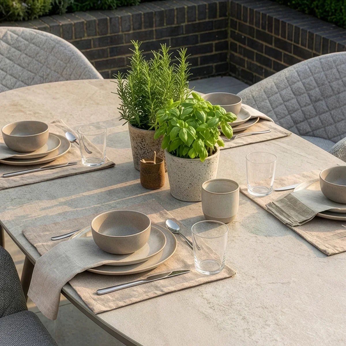 Outdoor dining table set with stoneware plates, neutral placemats, and potted herb centerpieces