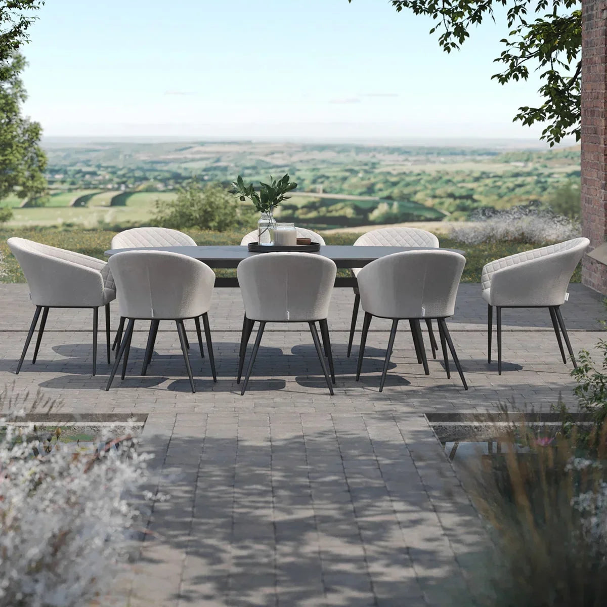 Outdoor dining set with eight grey upholstered chairs and rectangular table on stone patio