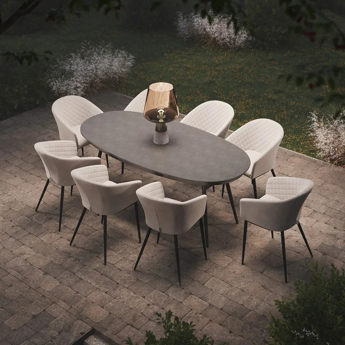 Outdoor dining set with oval stone table, eight cream armchairs on patio, modern lamp centerpiece