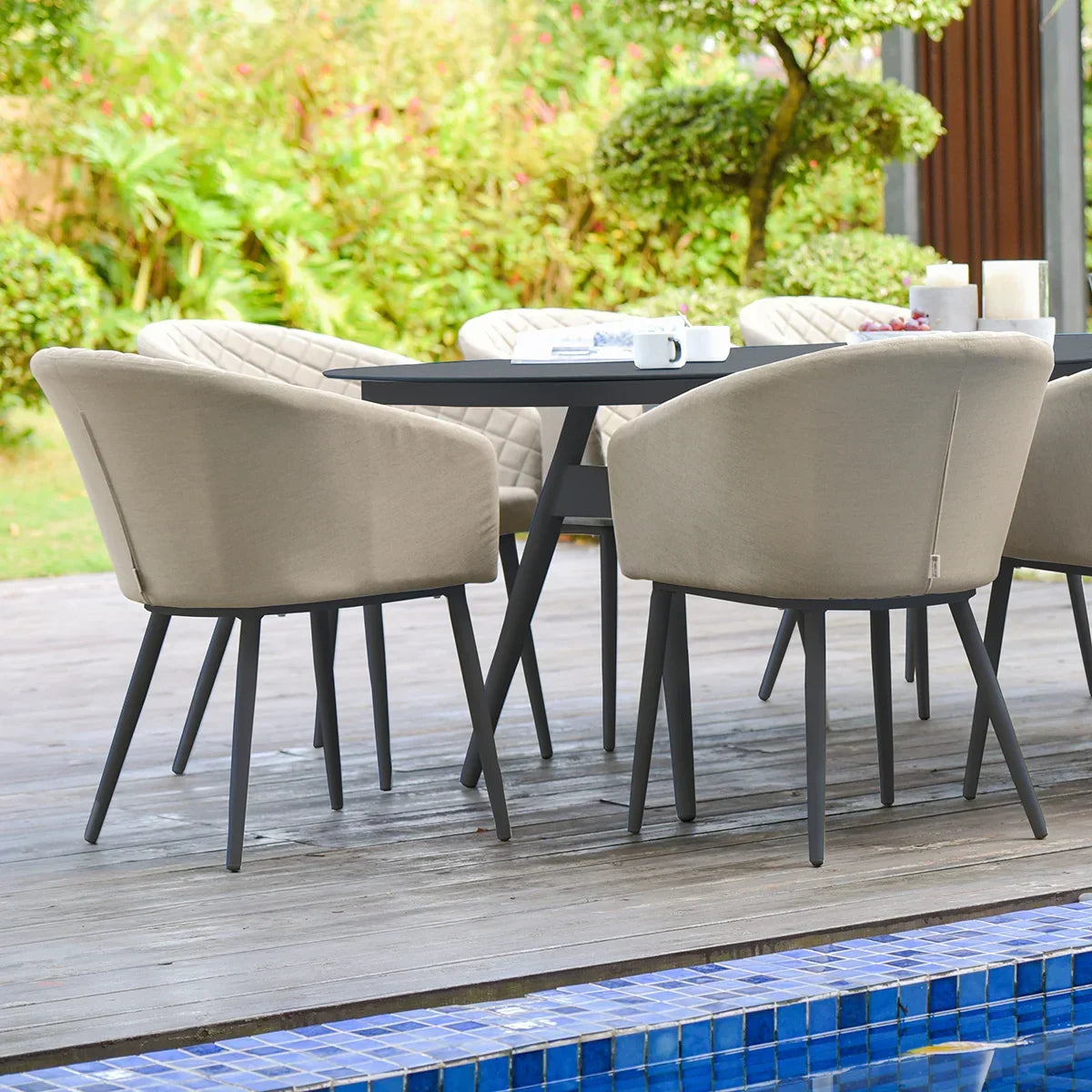 Outdoor dining set with beige cushioned chairs and black table on wooden patio by pool