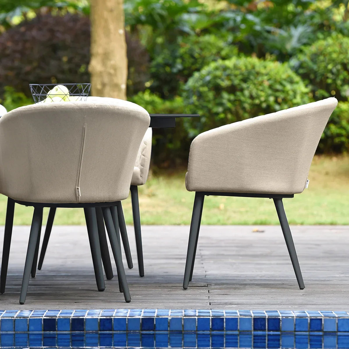Beige outdoor dining chairs with black legs beside a garden and blue-tiled patio