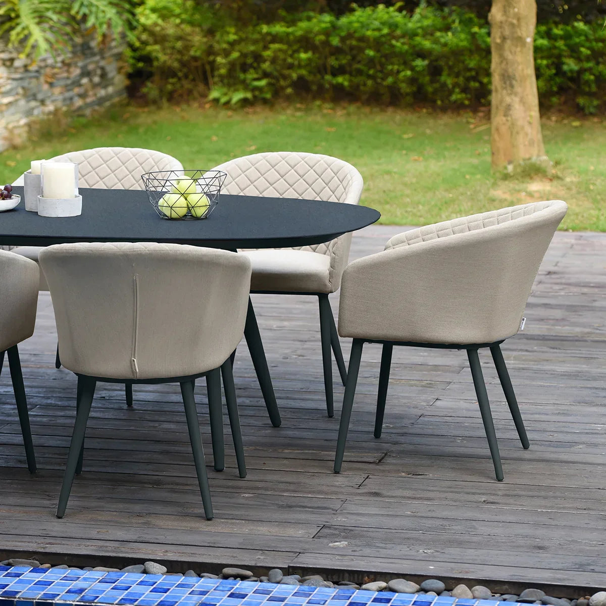 Outdoor dining set with six beige cushioned chairs and black oval table on wooden decking