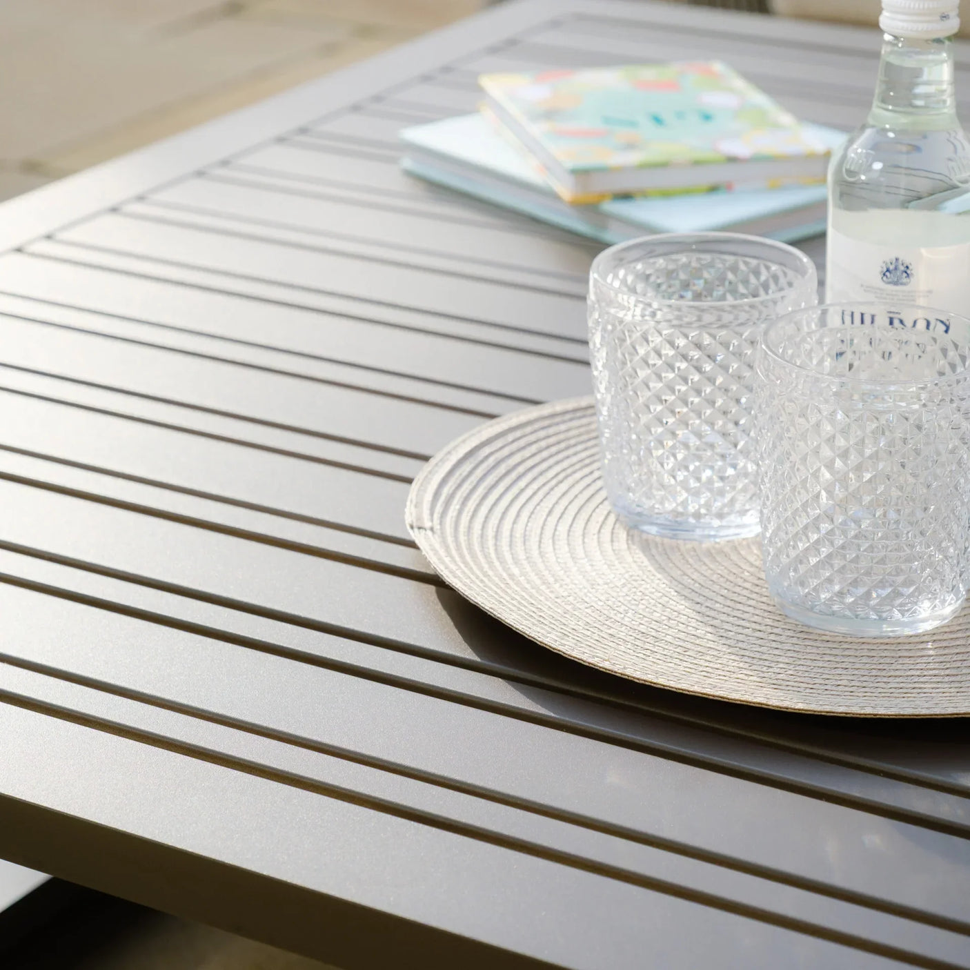 Grey slatted garden table with two textured glasses and a water bottle on round placemat