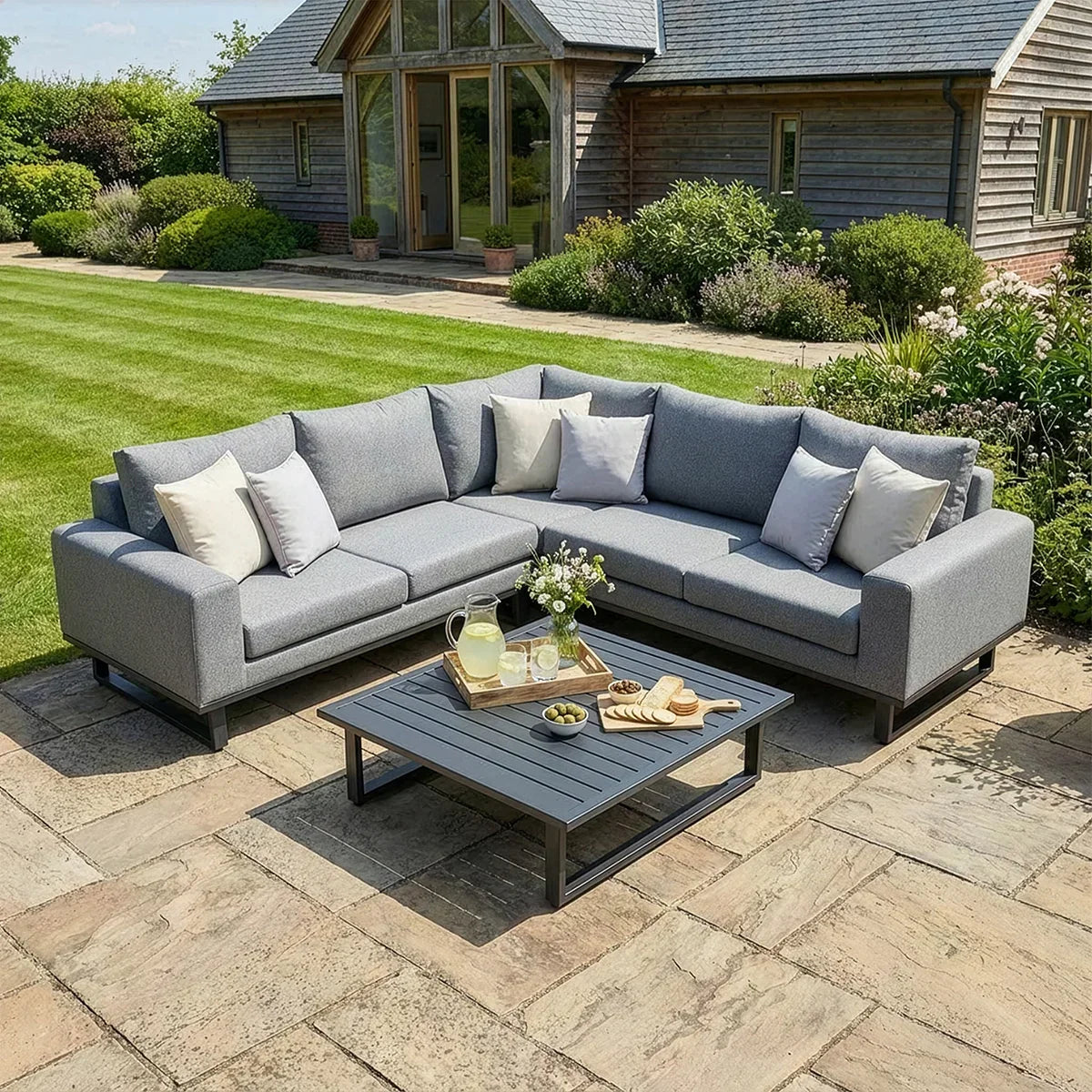 Grey outdoor corner sofa with cushions and coffee table on stone patio in garden setting