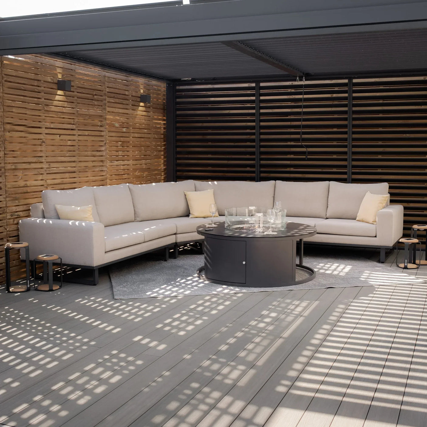 Beige outdoor corner sofa set with cushions and round fire pit table on covered decking