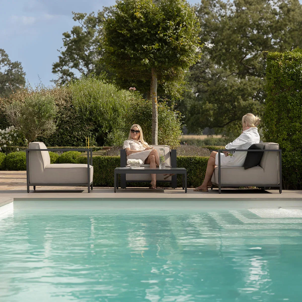 Outdoor sofa set with grey cushions and coffee table by poolside in a garden