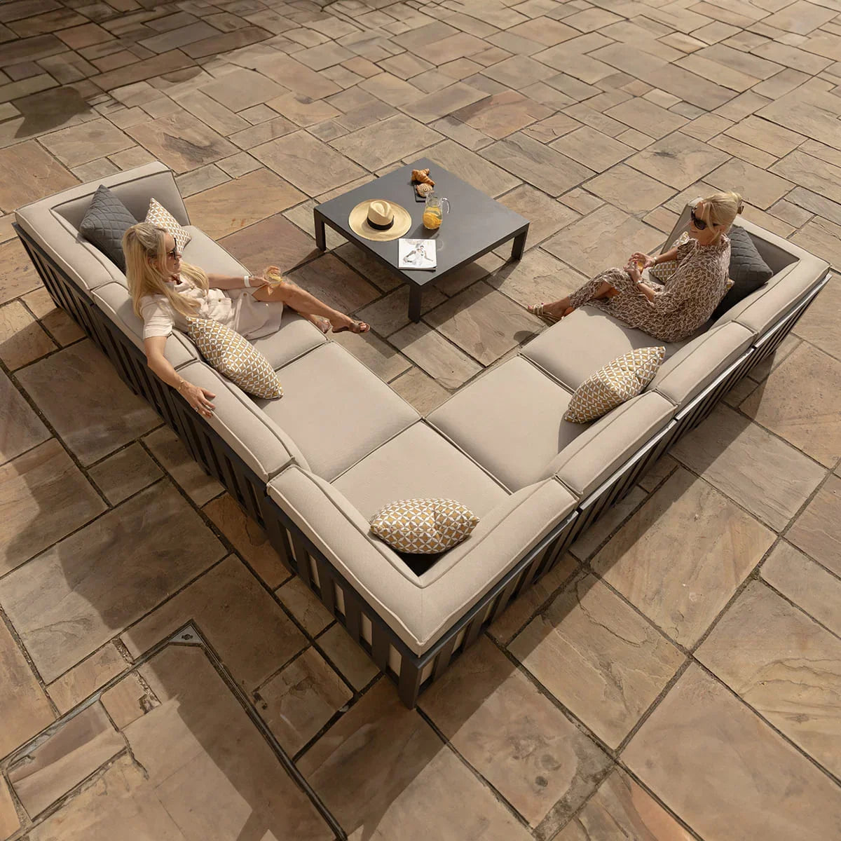 Beige outdoor corner sofa set with scatter cushions and coffee table on stone patio