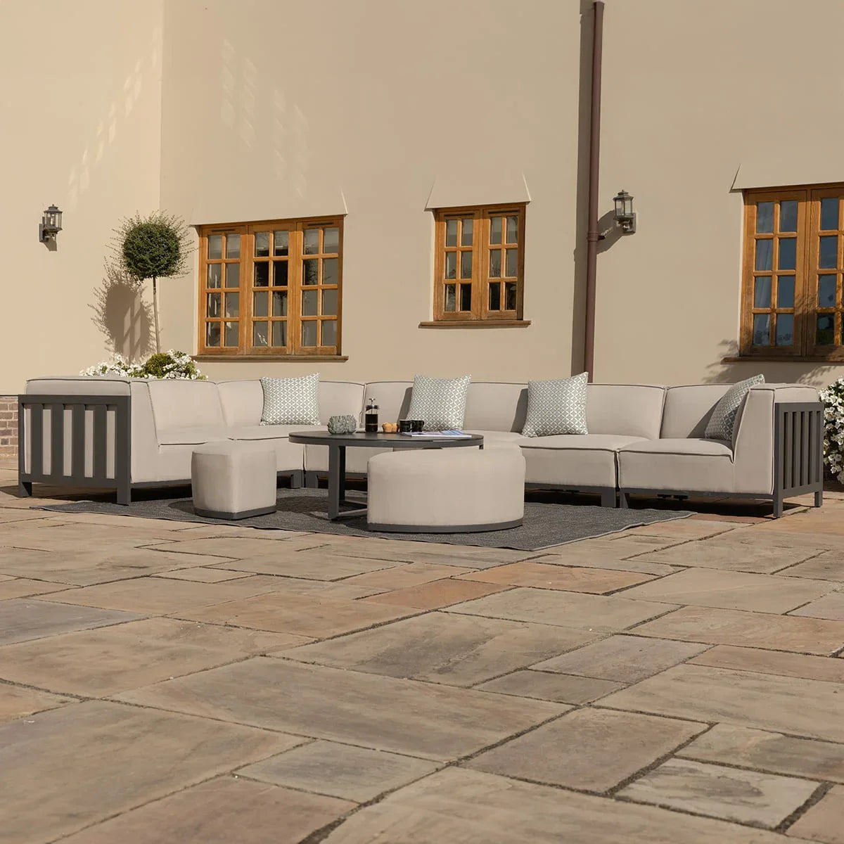 Light grey outdoor corner sofa set with coffee table and stools on stone patio