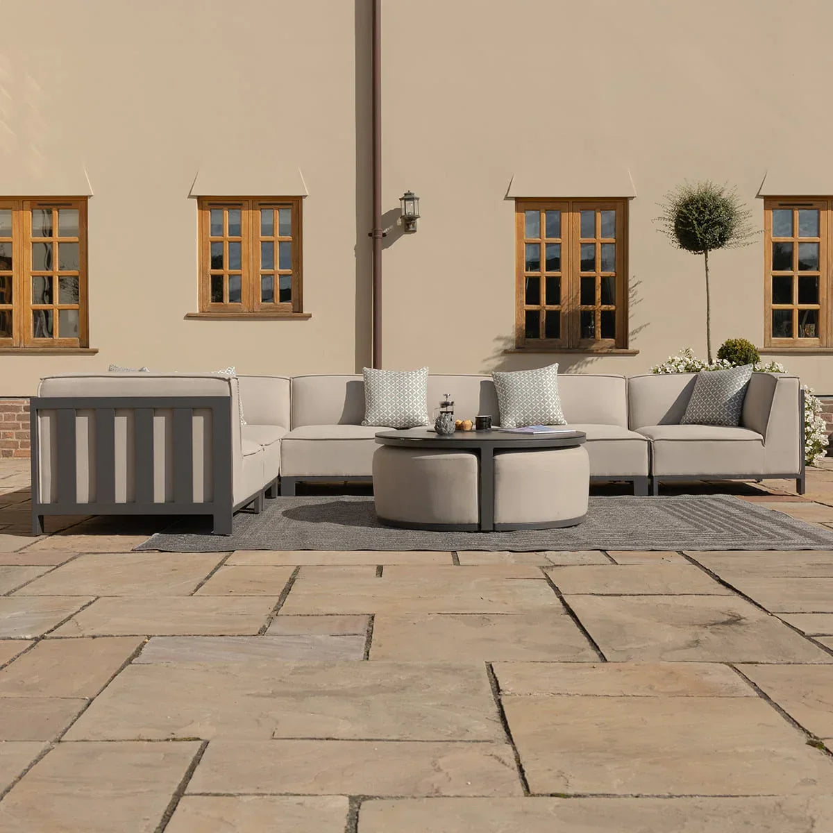 Outdoor corner sofa set with beige cushions, round coffee tables, and patterned pillows on patio