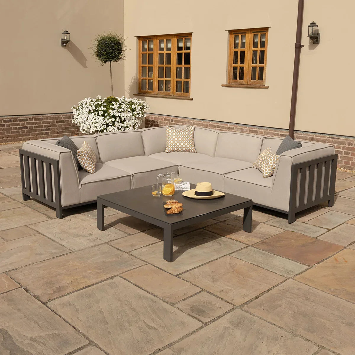 Outdoor corner sofa set with grey cushions and coffee table on a stone patio