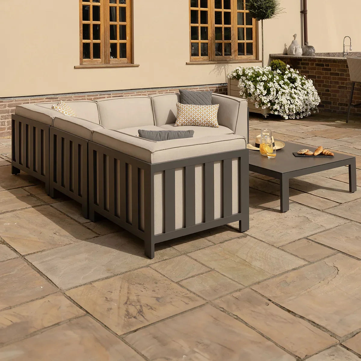 Outdoor corner sofa set with grey metal frame, beige cushions, and coffee table on patio