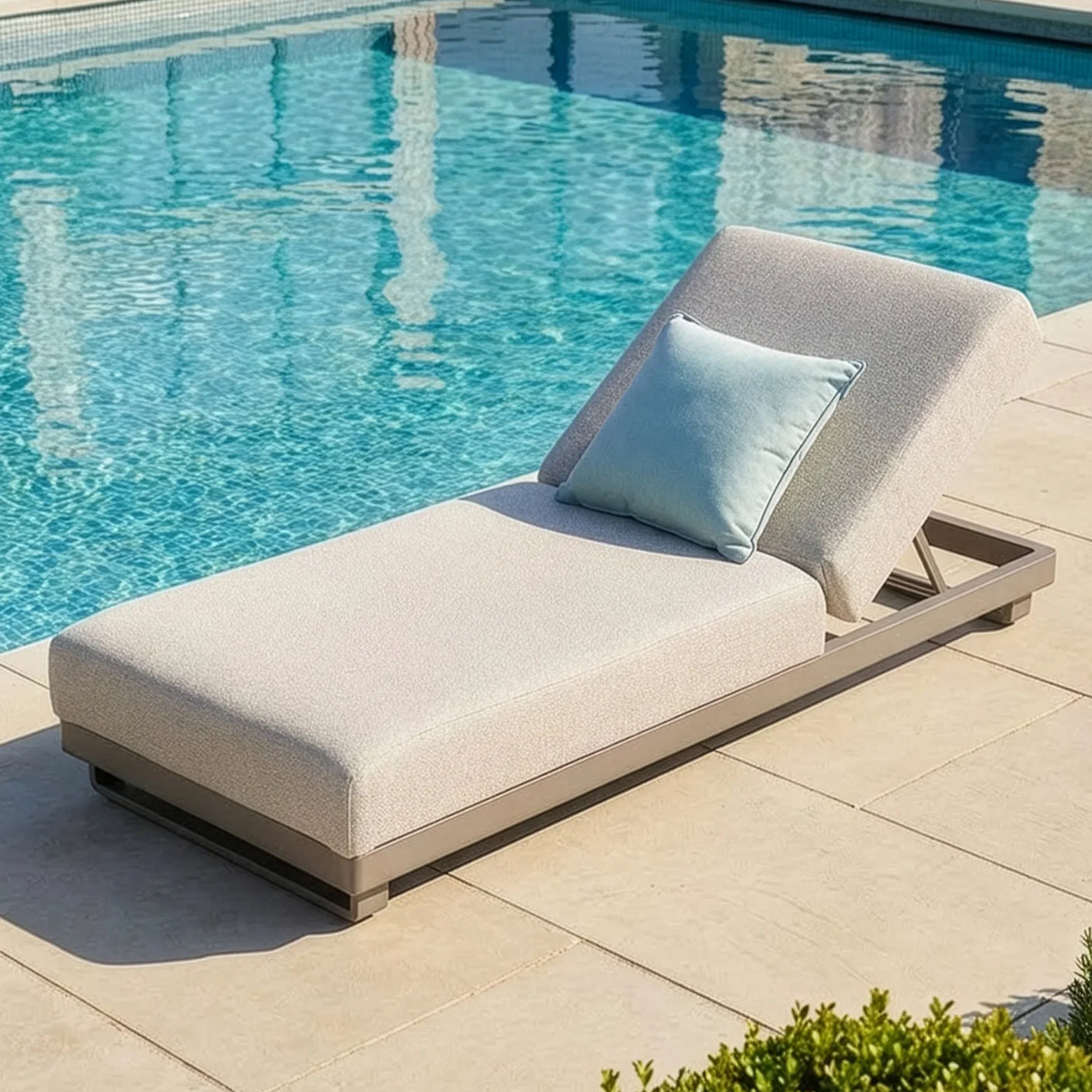 Outdoor sun lounger with light grey cushion and blue pillow beside a swimming pool
