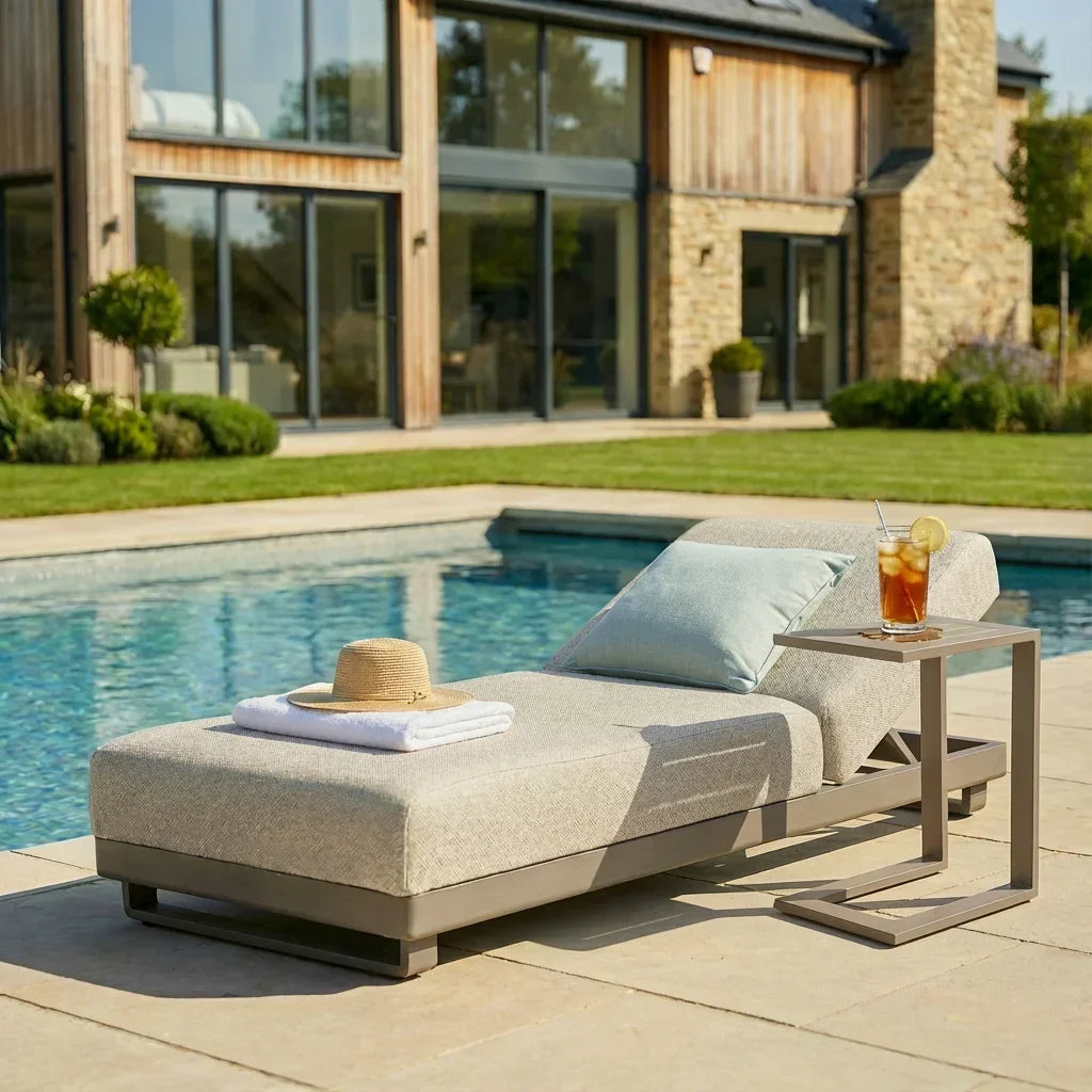 Outdoor fabric sun lounger with cushion by pool, side table holding iced drink and lemon slice