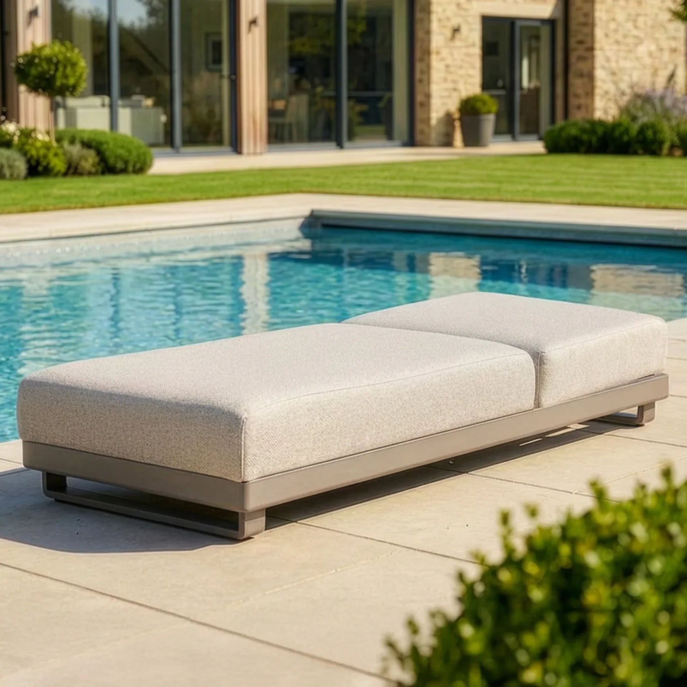 Outdoor fabric sun lounger with grey cushions by a pool on a stone patio