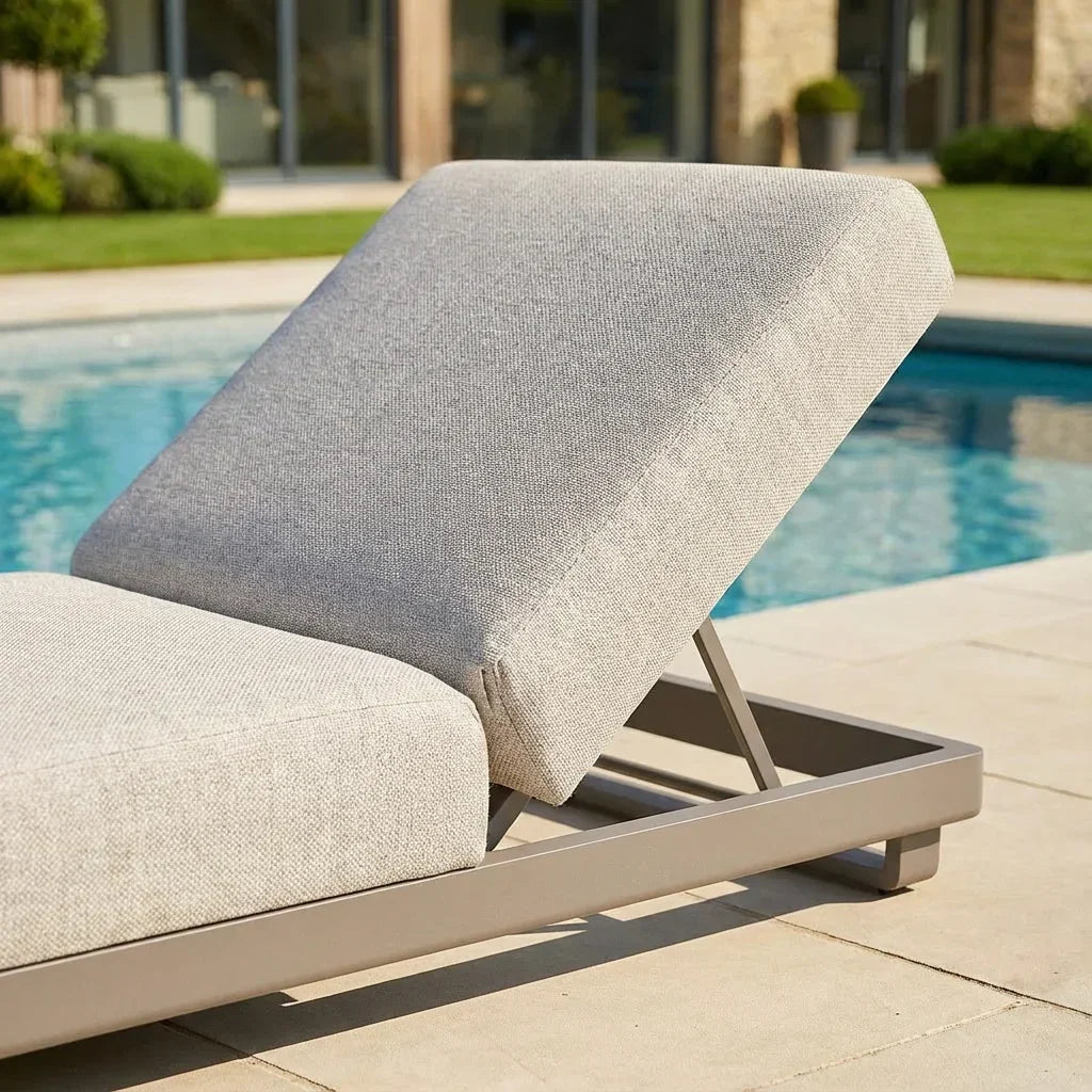 Light grey outdoor sun lounger with fabric cushions beside a swimming pool on patio