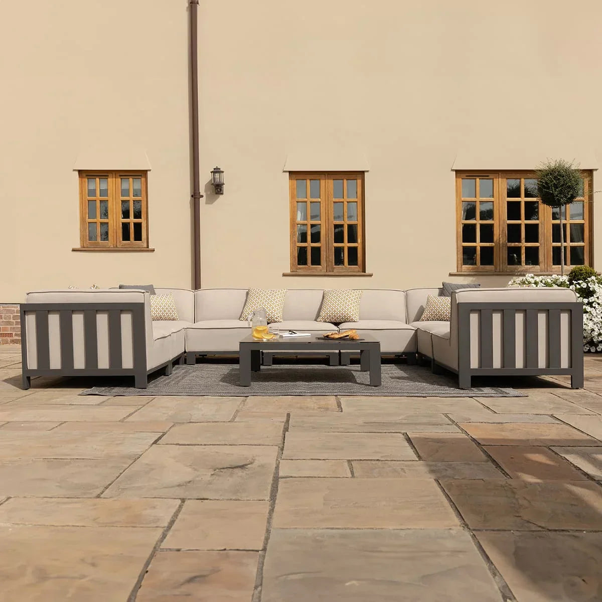 Grey outdoor corner sofa set with cream cushions and coffee table on patio