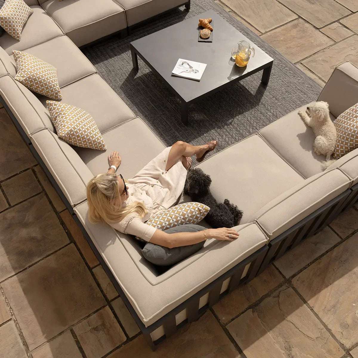 Beige outdoor corner sofa set with patterned cushions on patio, coffee table in center