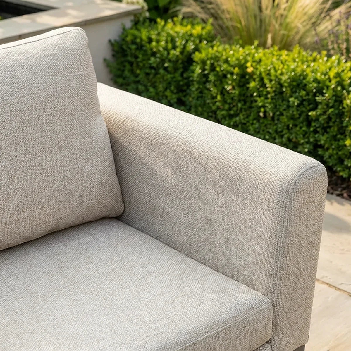 Light grey outdoor sofa corner with textured fabric and cushion in garden setting