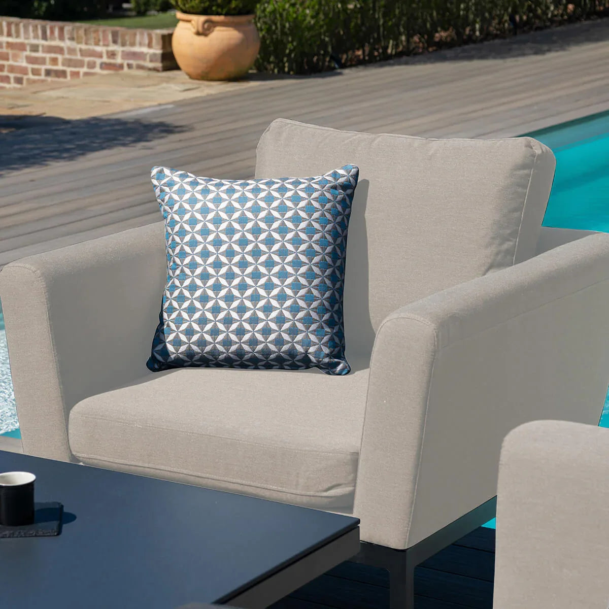 Outdoor armchair with light grey cushions and geometric blue scatter cushion by a pool