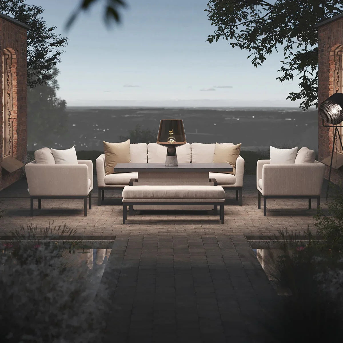 Cream outdoor sofa set with table, bench and armchairs on a stone patio at dusk